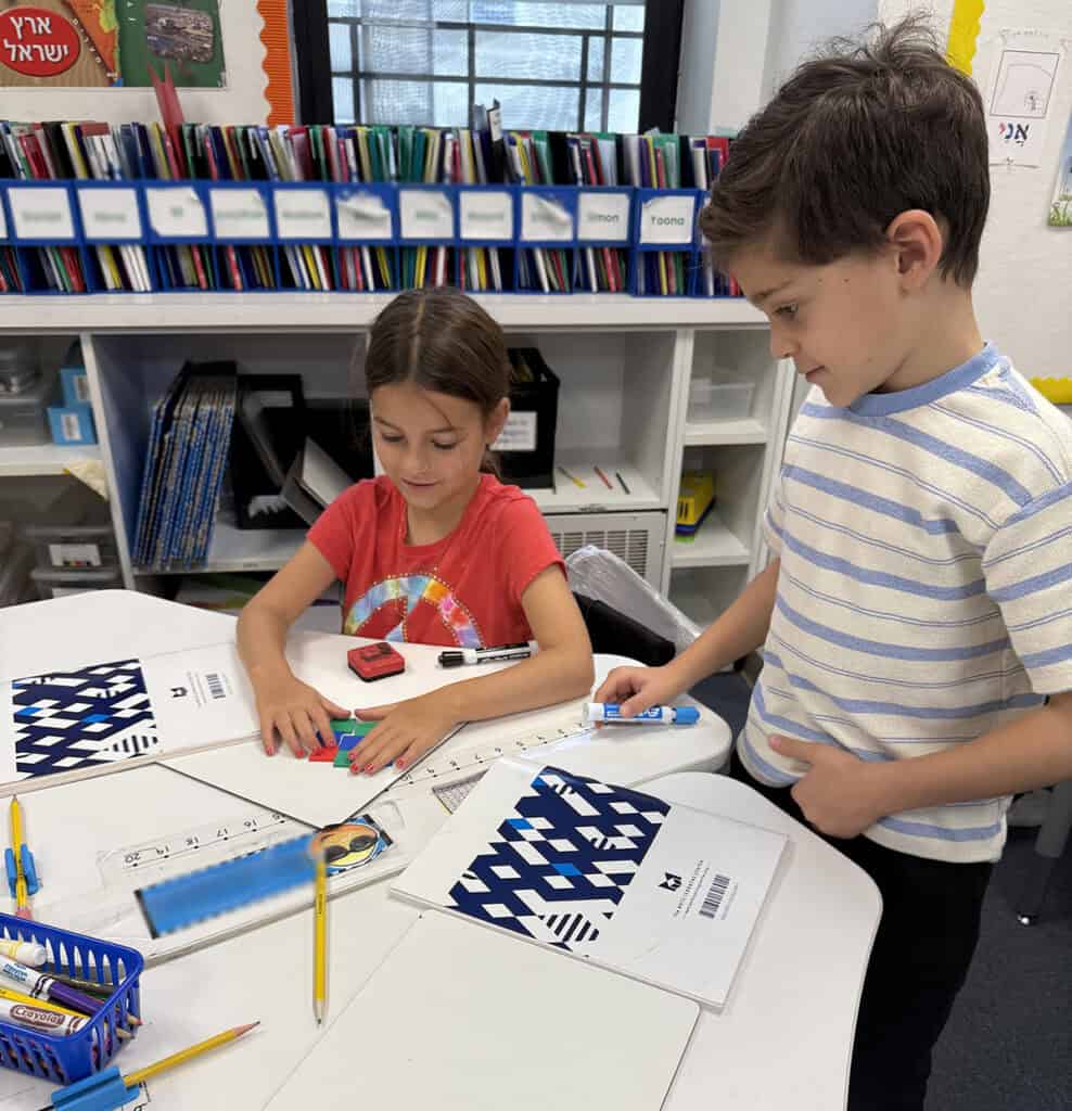 Elementary-age boy and girl at table with school supplies and geometric shapes practicing math concepts