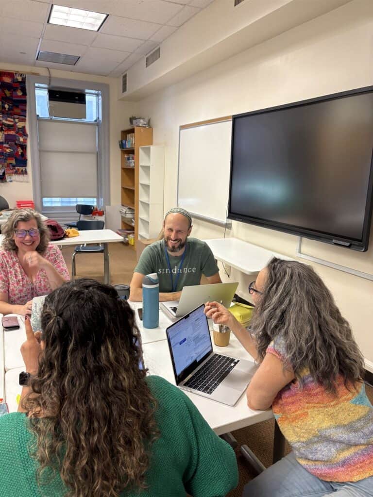 Teachers with computers sitting around a table in a classroom